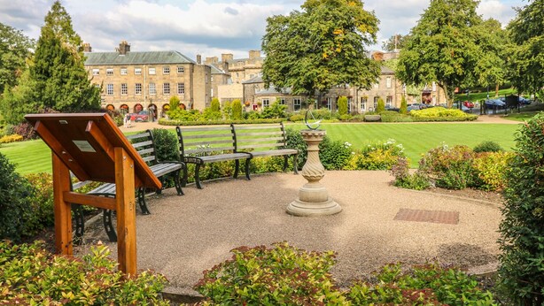 A courtyard with benches, a sundial, and a lawn. - The Haven (Buxton)