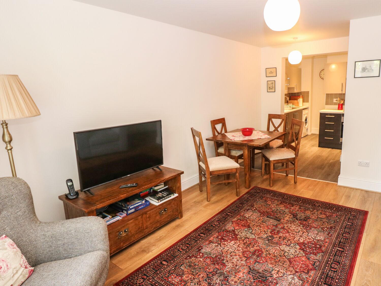 Un salon avec un téléviseur à écran plat posé sur un meuble en bois, une table à manger avec des chaises, un bol rouge et un tapis à motifs.
