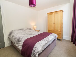 A bedroom with a bed, a wooden wardrobe, a bedside lamp, and a purple hanging light fixture. - The Haven (Buxton)