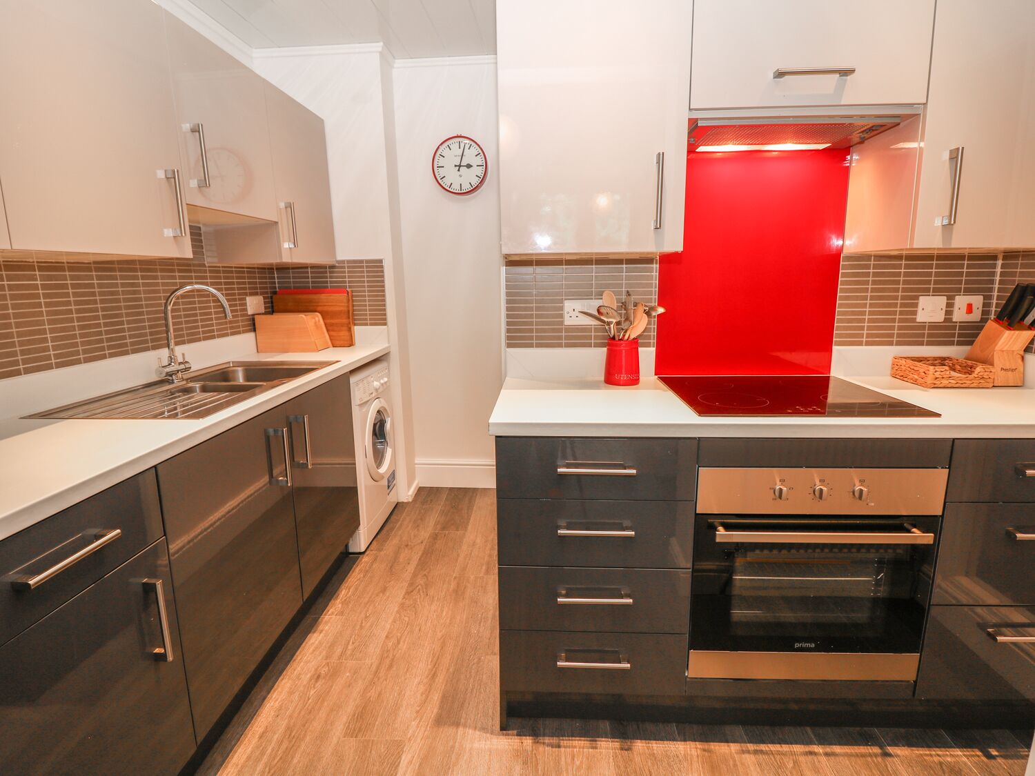 A modern kitchen with a built-in washing machine, a red induction cooktop, and a clock on the wall.