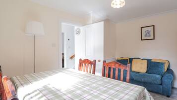Quarto com cama, uma poltrona, um sofá, uma luminária e uma porta que dá para outro cômodo.