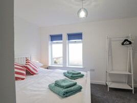 A bedroom with a bed, two windows with blue blinds, a white radiator, a hanging clothes rack, and a grey carpet.