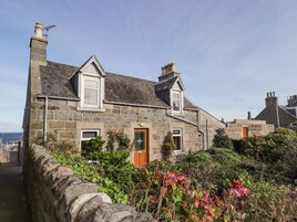 A stone house with a sloped roof, a chimney, and a small garden with flowering plants.