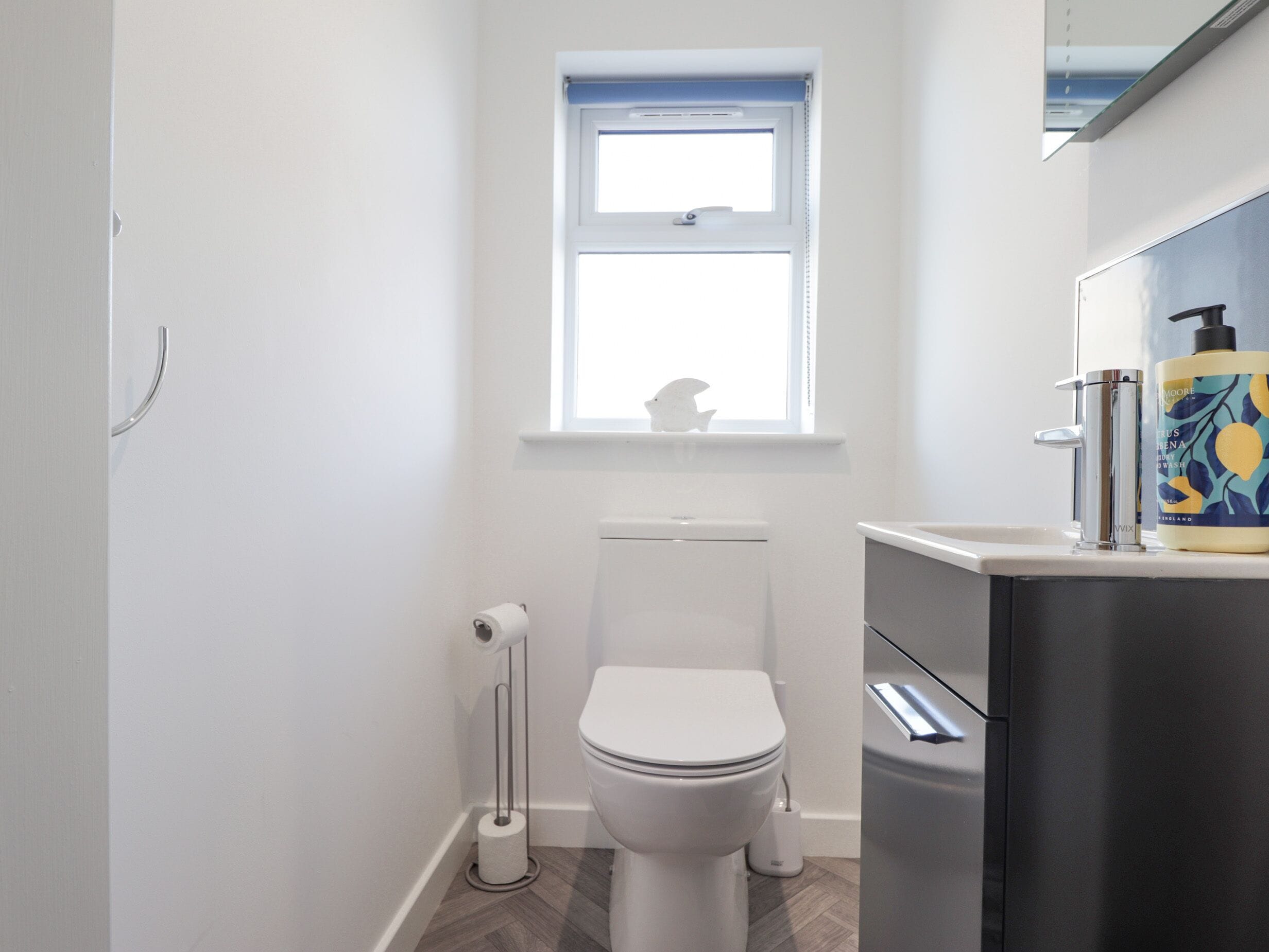 Ein modernes Badezimmer mit Toilette, einem Fenster und einem Waschbecken mit Seifenspender.