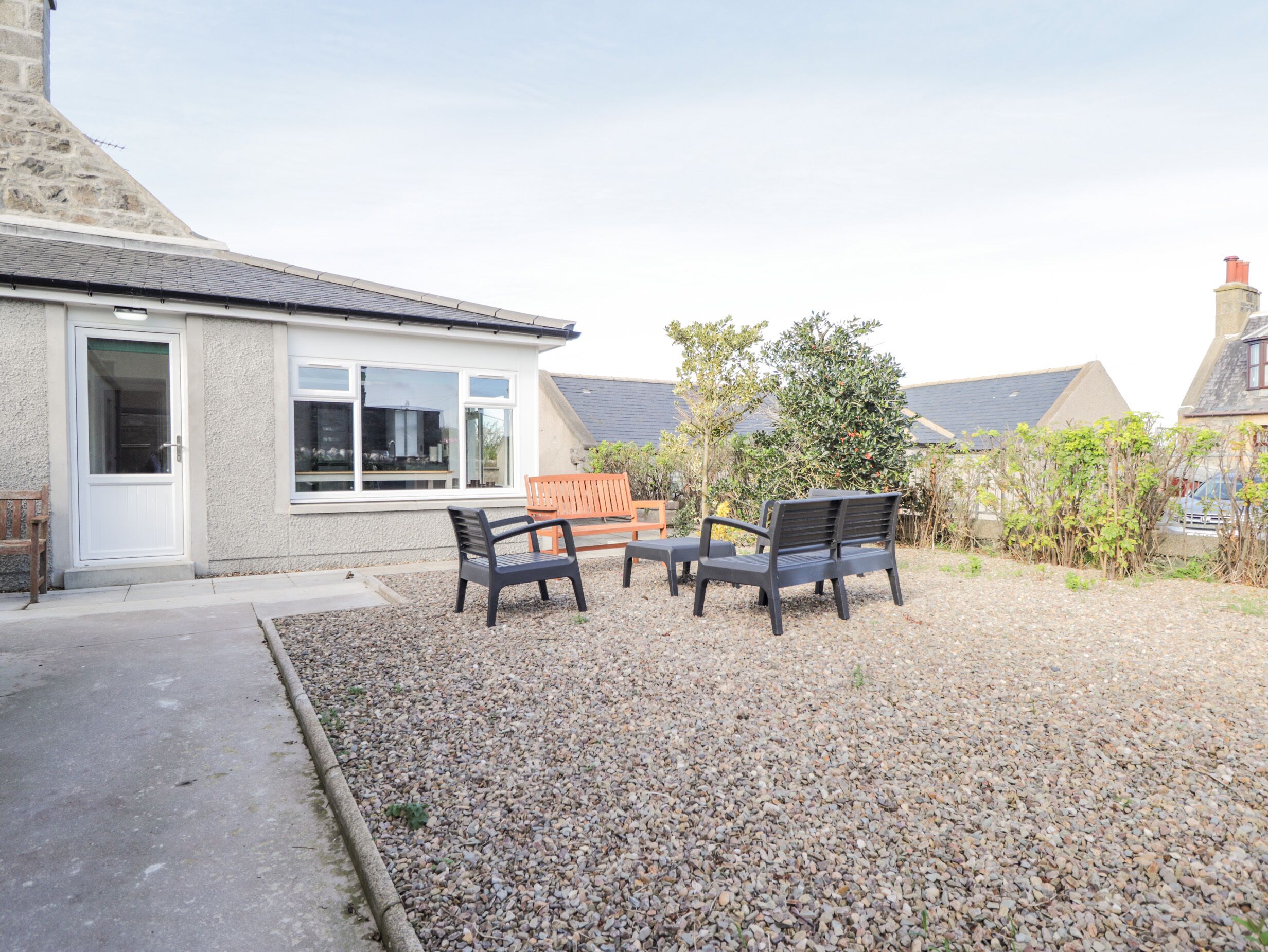 A residential property with a gravel driveway, a wooden bench, and a small garden area.