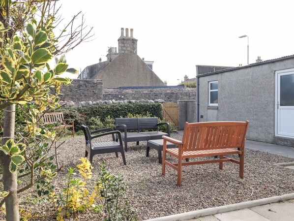 A garden with a stone wall, a wooden bench, and a table. - 19 Reidhaven Street (Banff)