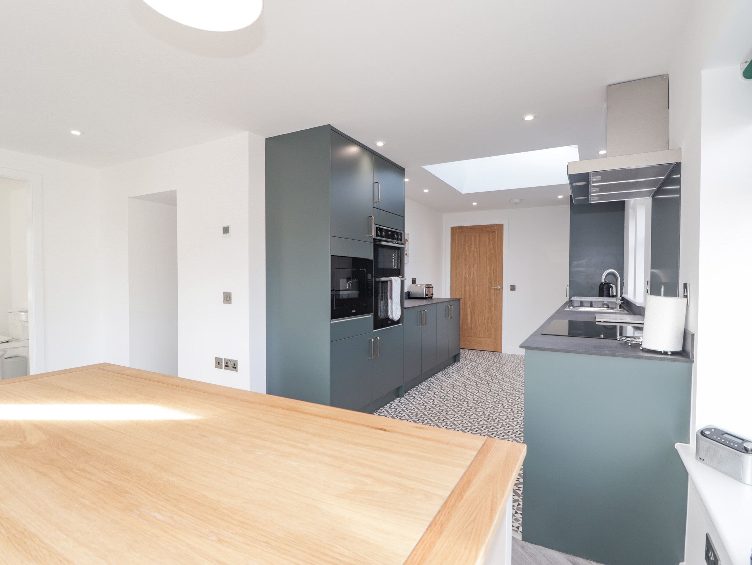 A modern kitchen with a wooden dining table, a built-in oven, and a small island with a sink.