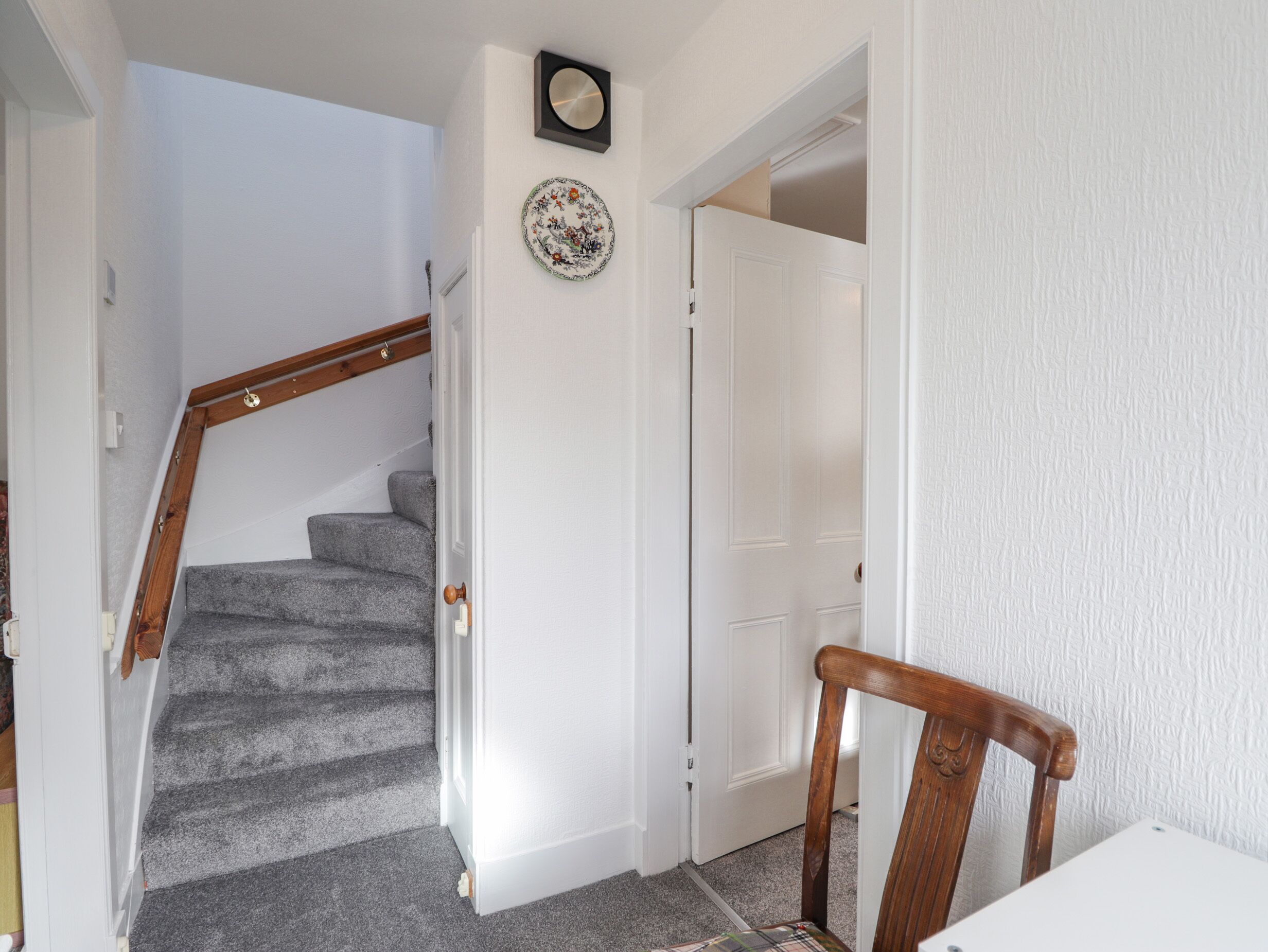 A staircase with carpeted steps leading to a white door. A wooden chair is positioned near the door.
