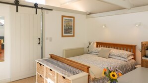 A bedroom with a bed, a radiator, a wooden headboard, a bedside table, a lamp, a picture frame, and a window. - The Daffodil Shed (Yelverton)