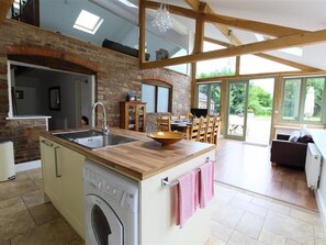 A kitchen with a built-in washing machine, a wooden countertop, and a dining area with chairs and a table. - The Old Mill (Mitcheldean)