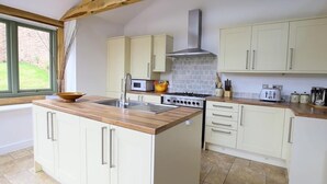 Cocina con armarios blancos, encimera de madera, estufa a gas, lavamanos y ventana con vistas a la vegetación.
