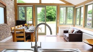 Cocina moderna con un lavamanos grande, mesa de comedor de madera y vistas a un jardín a través de amplios ventanales.