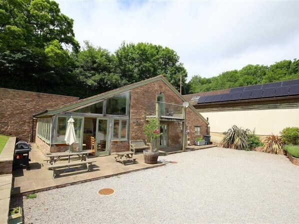 A modern building with a glass extension, outdoor seating, and a gravel driveway. - The Old Mill (Mitcheldean)