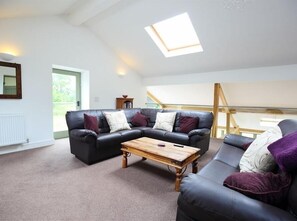 A spacious living room with a black leather sofa, a wooden coffee table, and a skylight. - The Old Mill (Mitcheldean)