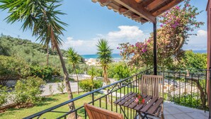 Un balcon avec une table et une chaise en bois, donnant sur un paysage côtier avec des arbres et une vue sur la mer.