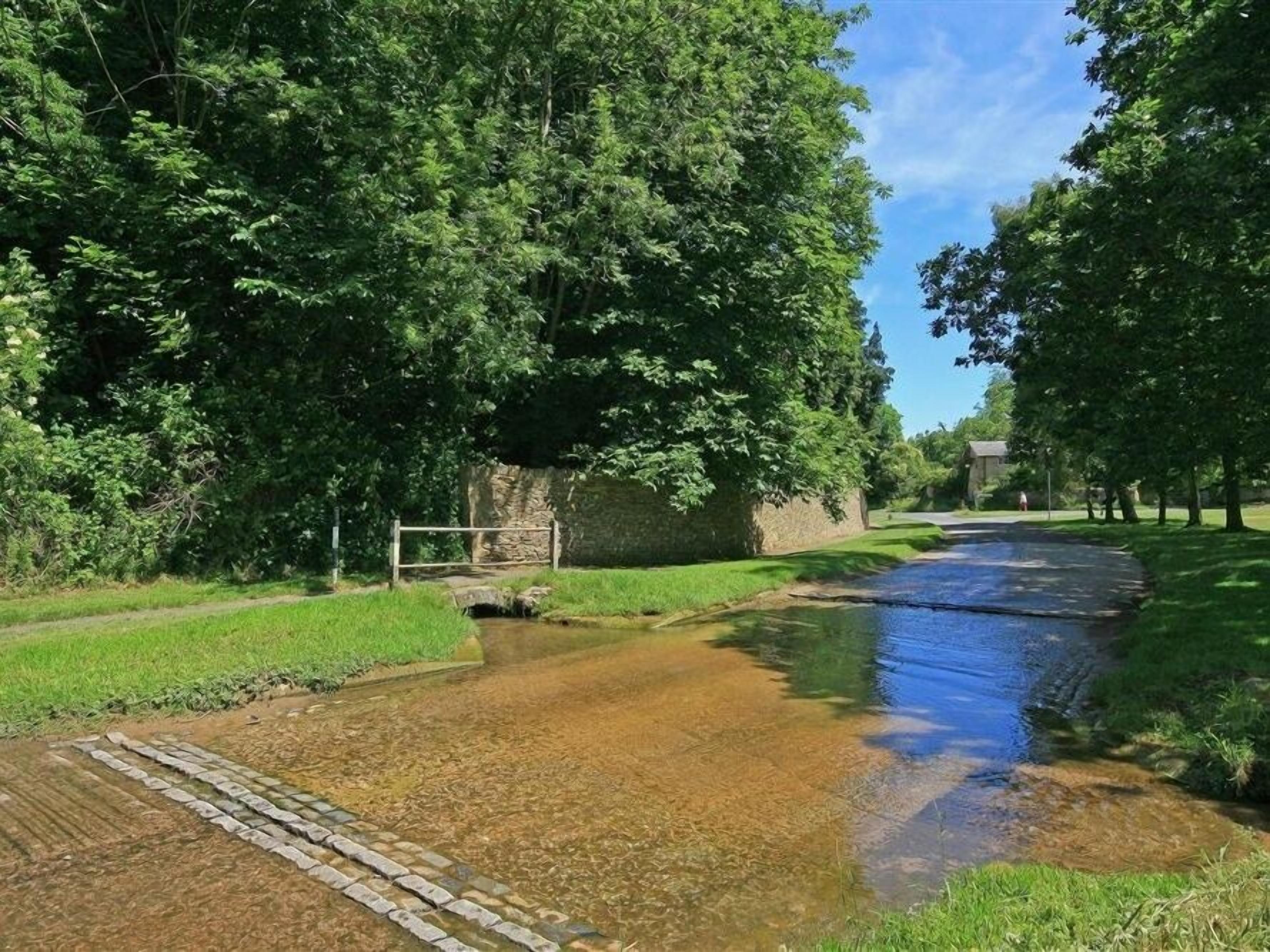 A rural landscape with a narrow water channel, grassy banks, and dense trees.