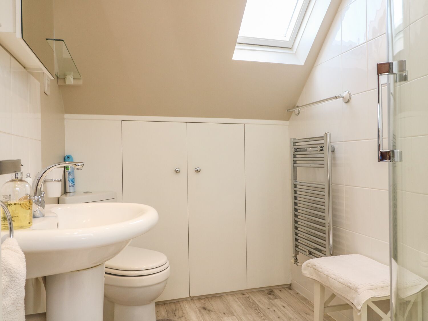 A modern bathroom with a skylight, a white sink, a toilet, and a glass shower enclosure.