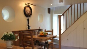 A dining area with a wooden table, chairs, and a fruit bowl. There is a staircase with wooden railings leading to an upper level. - The Folly at Castlebridge (Warminster)