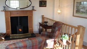 A cozy living room with a fireplace, a plaid armchair, a wooden staircase, and a framed picture on the wall. - The Folly at Castlebridge (Warminster)