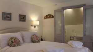 A hotel room with a neatly made bed, a bedside lamp, a mirror, and a door leading to a bathroom. - The Folly at Castlebridge (Warminster)