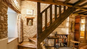 Eine rustikale Treppe mit Holzbalken und einem Holzgeländer, die zu einem Raum mit einer Steinwand, einer kleinen Ablage mit einer Vase und einem Bücherregal voller Bücher führt.