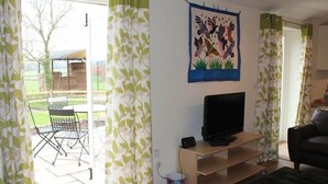 A living room with a TV on a wooden stand, a black sofa, and a green rug. - The Milking Parlour (Salisbury)