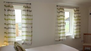 A bedroom with two beds, a wooden chair, and curtains with a striped pattern. - The Milking Parlour (Salisbury)