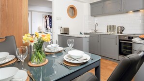 Una cocina moderna con armarios grises, horno empotrado y comedor con mesa de vidrio preparada para cuatro.