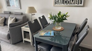 Una sala de estar moderna con una mesa de comedor, sillas, una lámpara, un cartel enmarcado y un florero con flores.