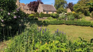 A traditional stone house with a well-maintained garden, including a lawn and various flowering plants. - Garden Cottage (Bampton)