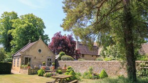A stone building with a garden, a picnic table, and a red flowering tree. - Garden Cottage (Bampton)