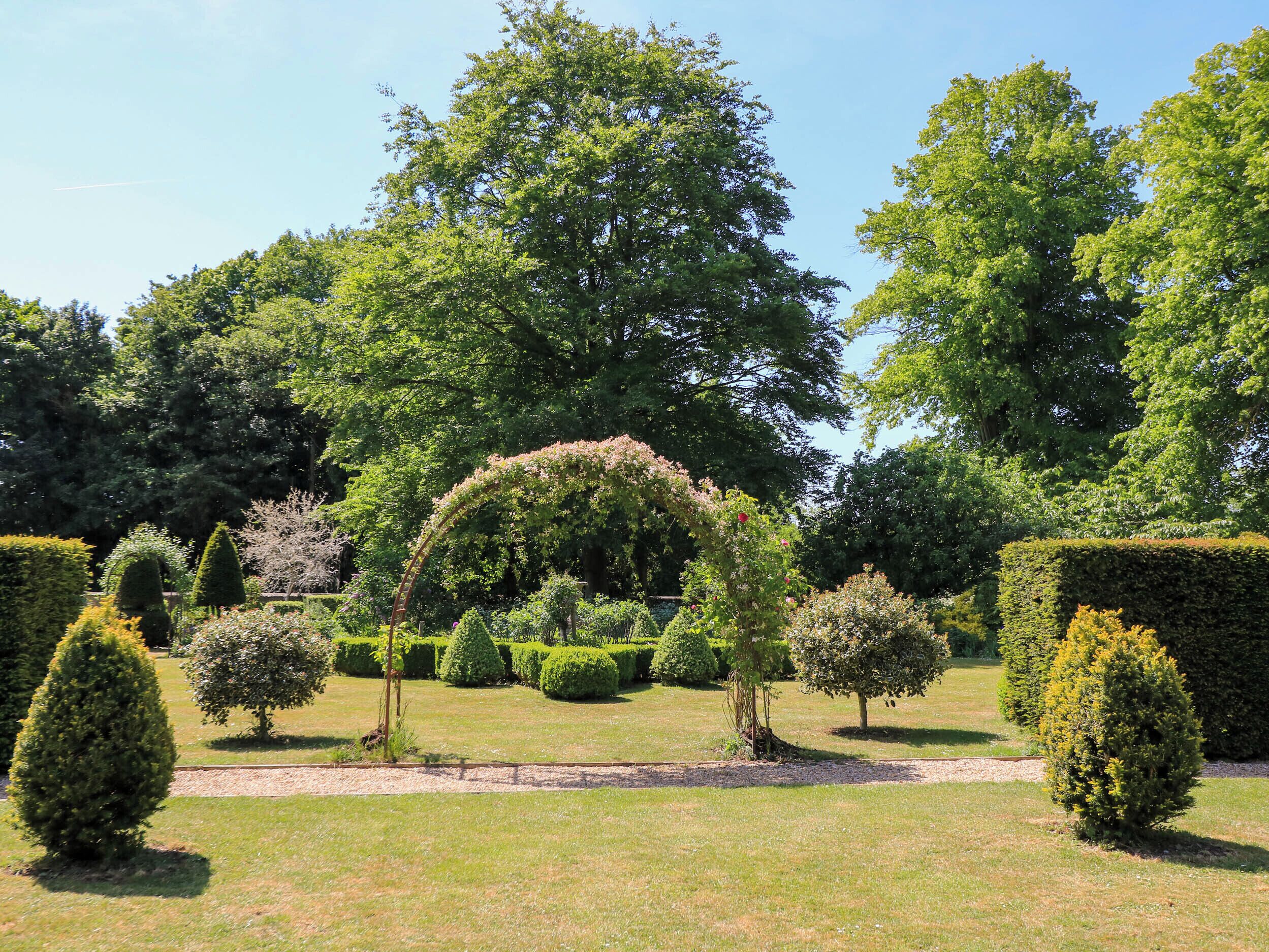 Ein gepflegter Garten mit ordentlich geschnittenen Hecken, verschiedenen Bäumen und blauem Himmel.