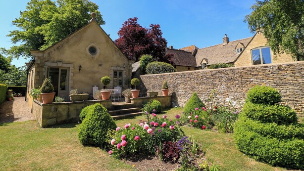 A stone house with a small garden, a patio with chairs, and a stone wall. - Garden Cottage (Bampton)