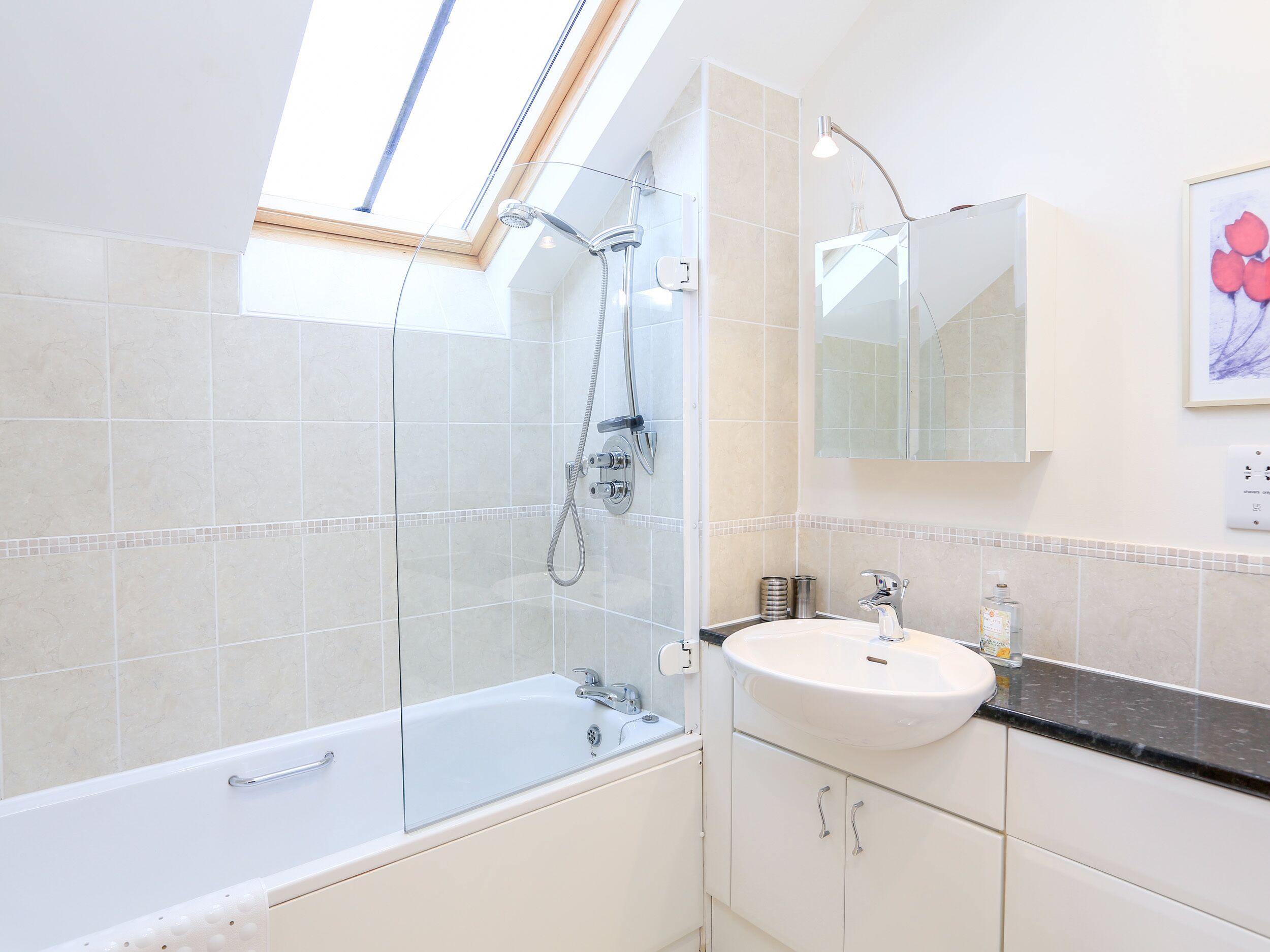 Une salle de bain moderne dotée d’une lucarne, d’une douche à parois de verre, d’une baignoire blanche et d’un lavabo avec un miroir au-dessus.