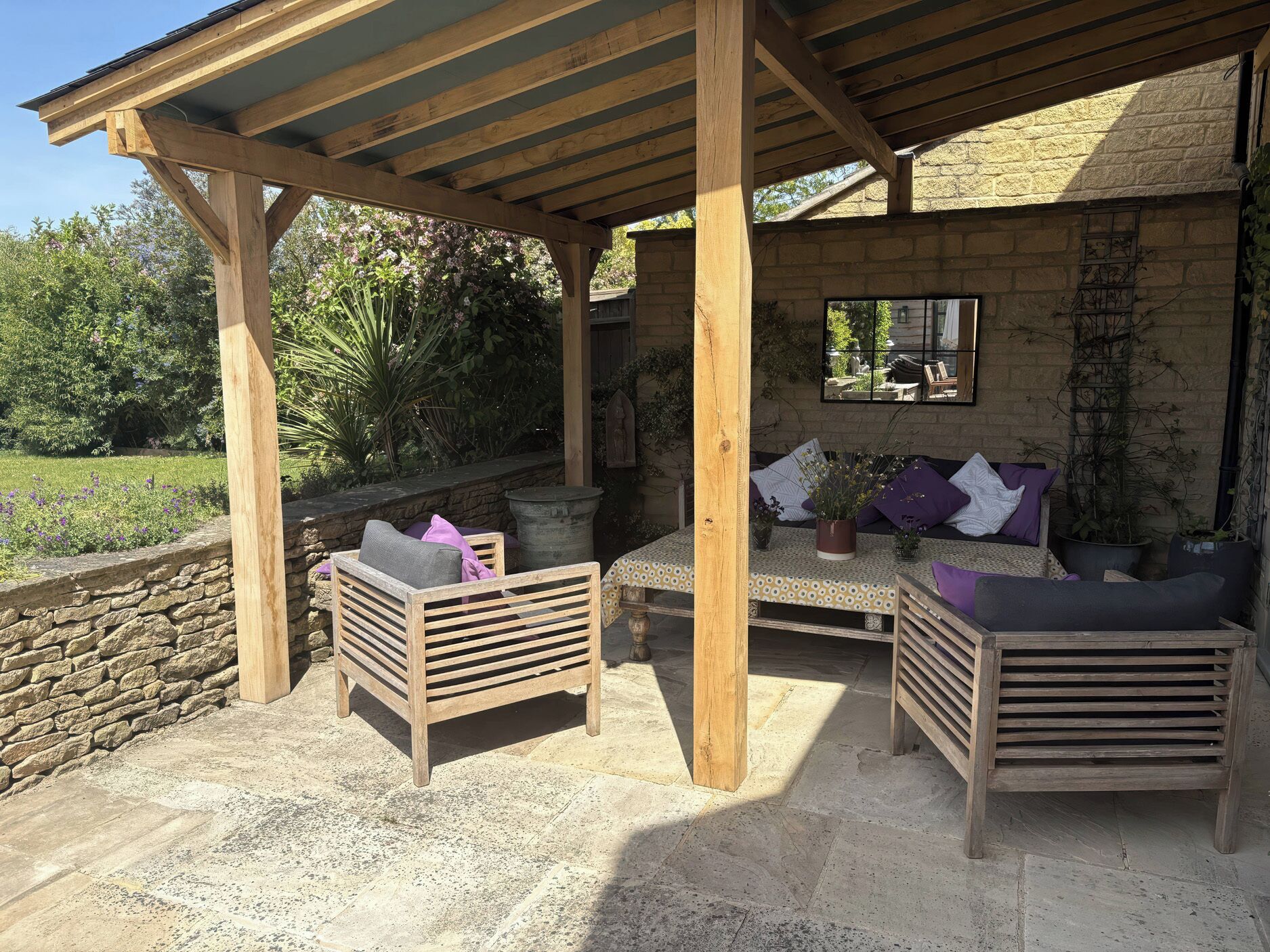 A covered outdoor seating area with wooden furniture and a stone wall backdrop.