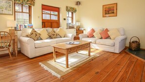 A living room with two sofas, a wooden coffee table, and a bookshelf. - The Coach House (Exmouth)