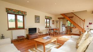 A spacious living room with a wooden staircase, a dining area, and a kitchen. - The Coach House (Exmouth)