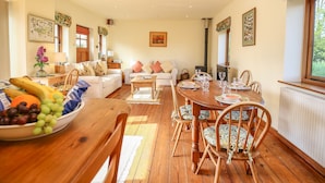 A cozy living room with a dining area, wooden furniture, and a fireplace. - The Coach House (Exmouth)