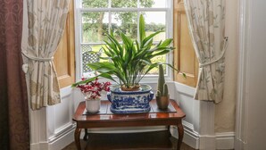 A room with a large window, a wooden table with a vase of flowers, and two potted plants. - Godscroft Hall (Frodsham)