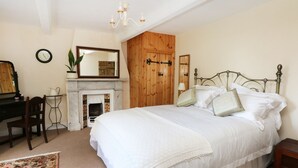A bedroom with a large bed, a wooden wardrobe, a desk with a chair, a fireplace, and a mirror on the wall. - Godscroft Hall (Frodsham)