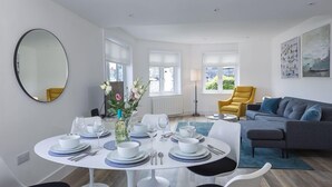Una sala de estar moderna con comedor, que incluye una mesa redonda para cuatro personas, un sofá y un espejo grande en la pared.