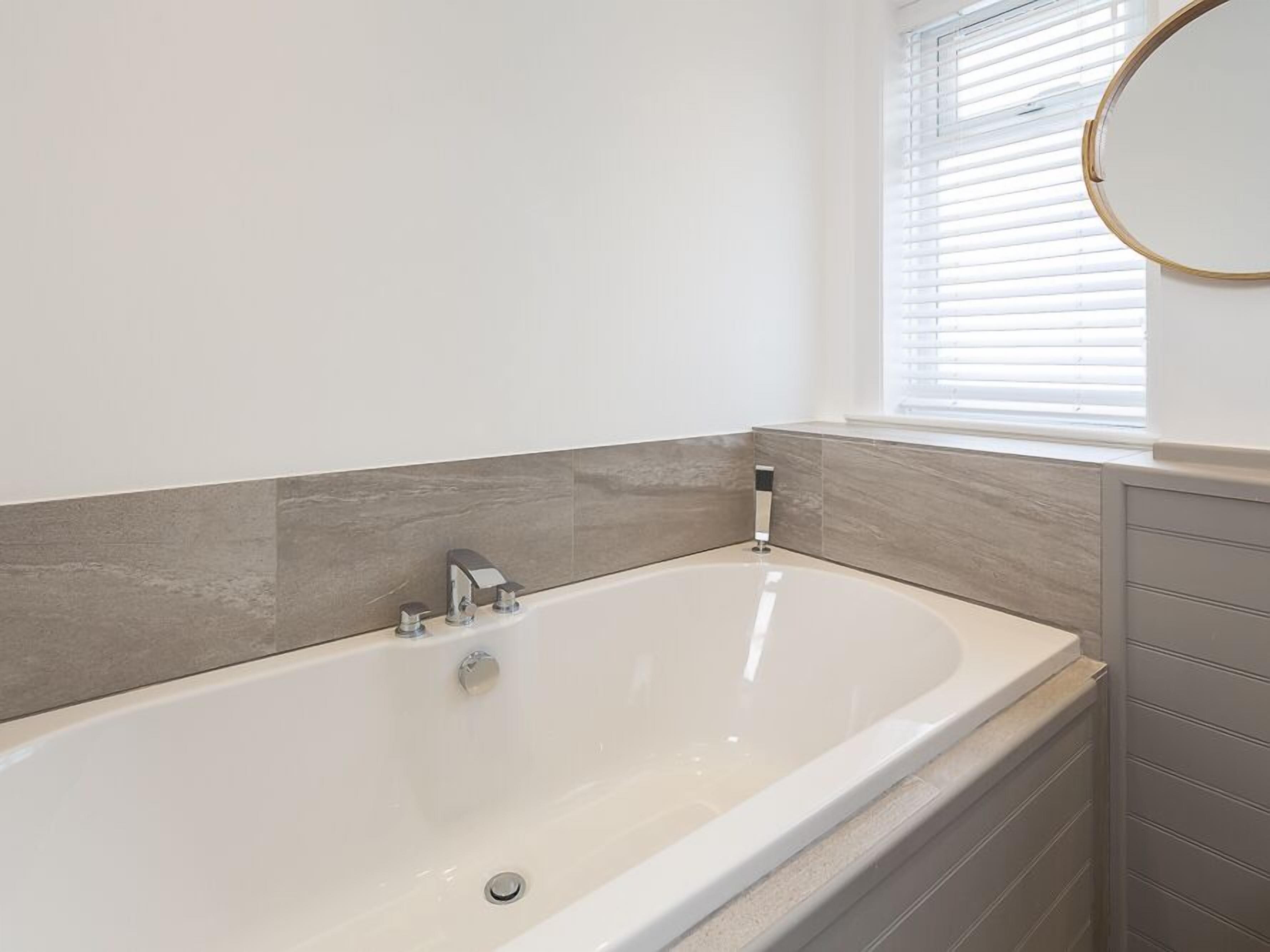 A modern bathroom with a freestanding bathtub, a window with blinds, and a wall-mounted mirror.