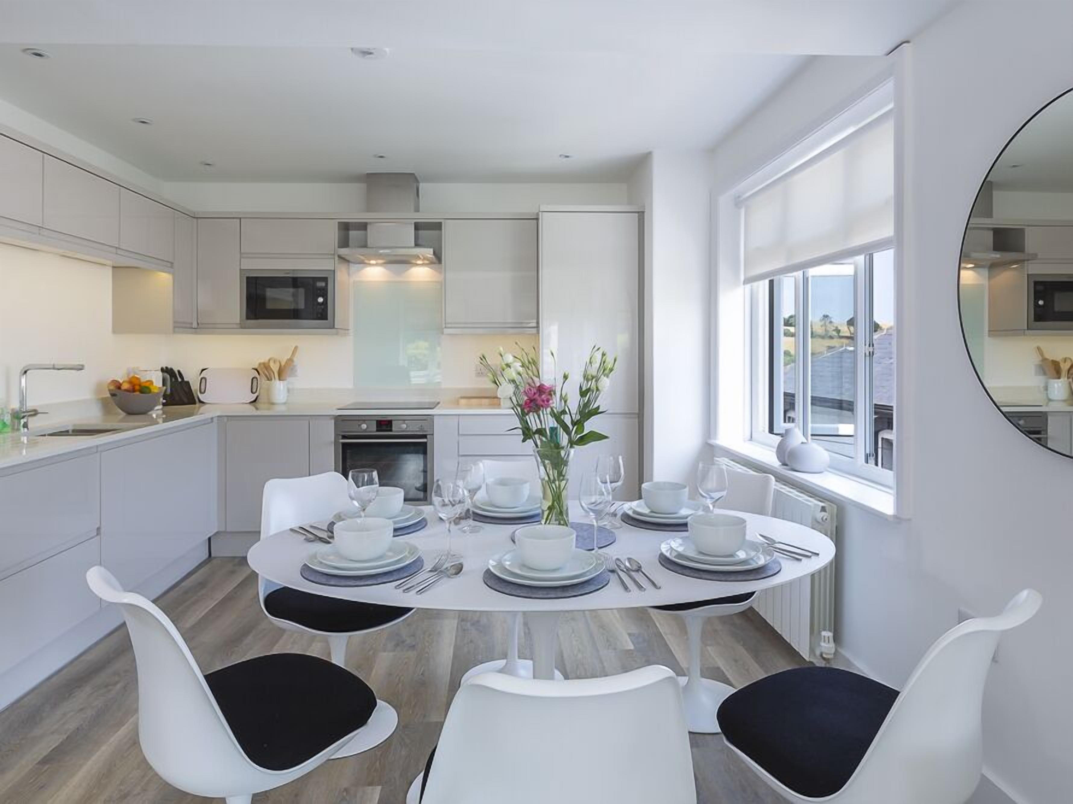 A modern kitchen with white cabinetry, a dining table set for four, and a large window providing natural light.
