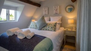 Un dormitorio con una cama, almohadas, una mesita de noche con una lámpara, una ventana y un espejo en la pared.