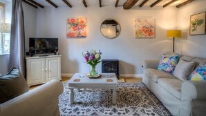 Una sala de estar acogedora con vigas de madera a la vista, una chimenea, un televisor y un sofá con cojines de colores.