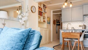 A modern living room with a blue sofa, a dining area with a wooden table and chairs, and a kitchen with white cabinets and a tiled backsplash. - 36 The Salcombe (Salcombe)
