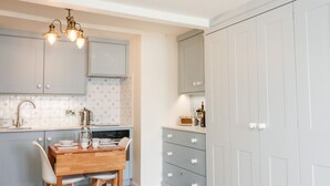 A kitchen with light blue cabinets, a wooden dining table, and a white cabinet with drawers. - 36 The Salcombe (Salcombe)