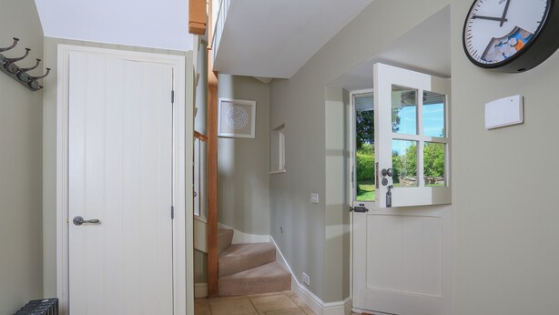 A hallway with a white door, a clock, and a view of a garden through a window. - Warren Cottage (Dartmouth)
