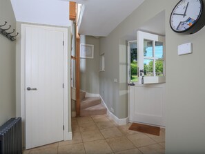 A hallway with a white door, a clock, and a view of a garden through a window. - Warren Cottage (Dartmouth)
