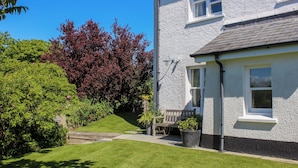A two-story house with a well-maintained lawn, a wooden bench, and a potted plant near the entrance. - Warren Cottage (Dartmouth)